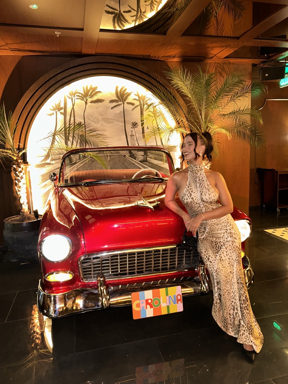 Andrea Mena en una escena de lifestyle junto a un auto clásico rojo